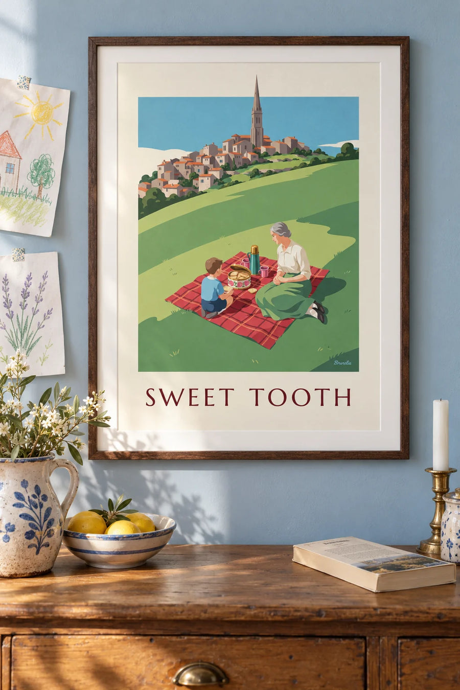 Poster of a picnic and a flowered cookie tin on a hill: framed on the wall